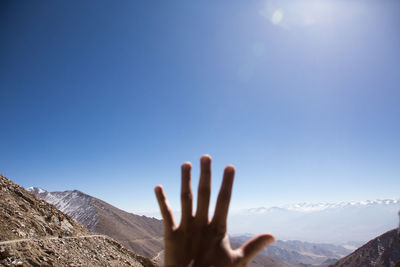 Cropped hand of person gesturing against mountains and sky during sunny day