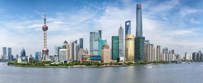 Modern buildings by river against cloudy sky in city