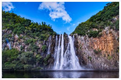 Scenic view of waterfall in forest against sky