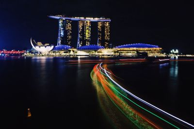 Light trails on river with marina bay sands in background at night