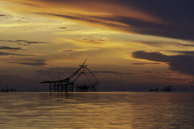 Silhouette sailboat on sea against dramatic sky during sunset