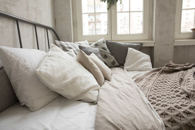 Bunch of soft cushions lying on soft bed near window in cozy room