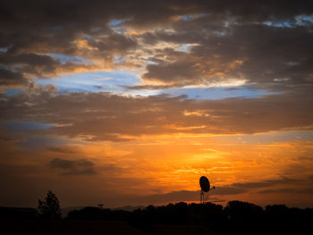 Silhouette trees on landscape against dramatic sky during sunset