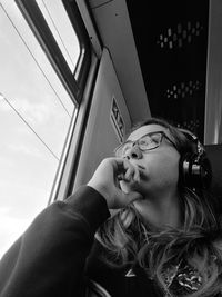 Low angle portrait of young woman looking through window