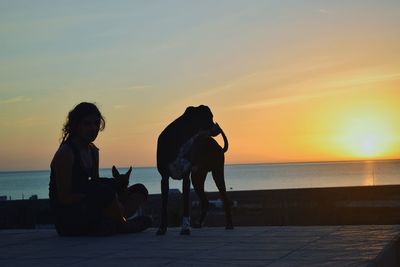 Silhouette people sitting on beach against sky during sunset