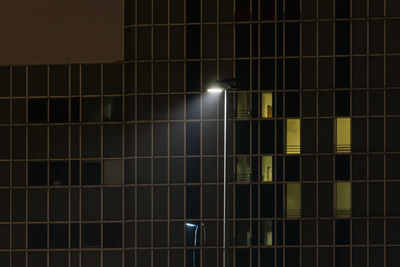 Low angle view of illuminated street light against modern building at night