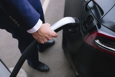 Businessman plugging in power cable of electric car at charging station