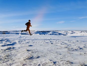 Full length of man running in snow covered land against sky