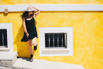 Full length of young woman standing leaning on yellow wall