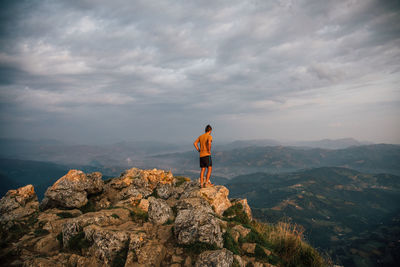 Rear view of man standing on rock against sky