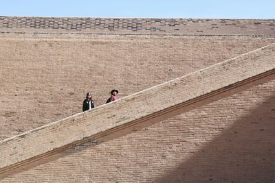 Low angle view of female friends on steps against wall