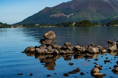 Rocks in lake by mountains against sky