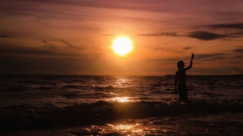 Silhouette boy standing at beach during sunset