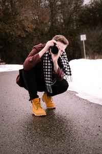 Young woman photographing while crouching on road during winter