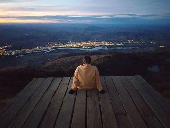 Rear view of man sitting on pier over sea against sky