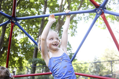 Happy cute girl climbing jungle gym against trees at playground