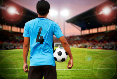 Rear view of soccer player holding ball while standing on field in stadium