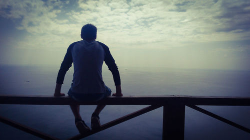 Rear view of man sitting on railing against sea