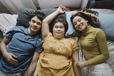 Directly above portrait of smiling siblings lying down with down syndrome sister on bed at home