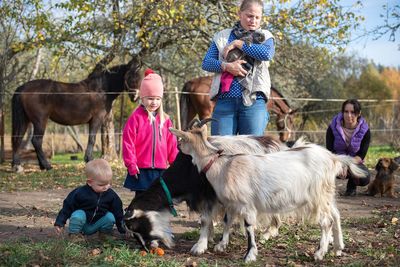 Happy family-mother with children hugging and feeds pets dogs, cats and goats in countryside farm