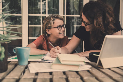 Happy woman teaching son sitting on table at home