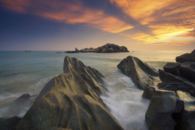 Rocks at sea against sky during sunrise