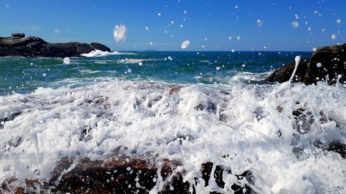 Waves splashing on rocks at shore against sky