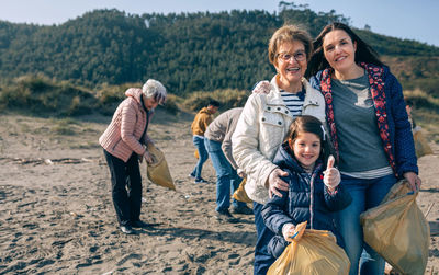 Portrait of confident female family standing at beach while cleaning garbage