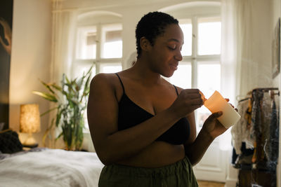 Smiling young woman holding lit candle in bedroom at home