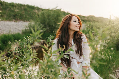 Beautiful young woman looking away by plants against sky