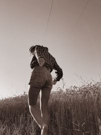 Rear view of woman walking by plants on field against clear sky