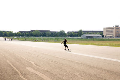 Rear view full length of girl skateboarding on street against sky
