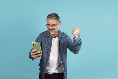 Young man using mobile phone while standing against blue background