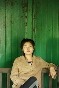 Portrait of beautiful young woman sitting on bench against wooden wall