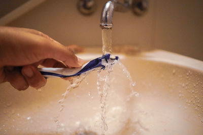 Close-up of hand washing razor in bathroom sink