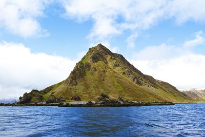 Scenic view of sea by mountain against sky