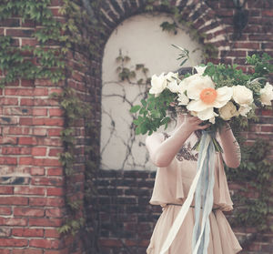 Low angle view of woman holding flower bouquet against wall