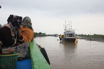 Rear view of men sitting on boat in river against sky