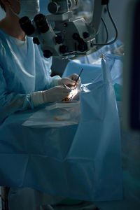 Crop anonymous eye surgeon with manual instruments operating patient on medical bed in hospital on blurred background