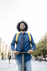 Portrait of smiling man with backpack on his e-scooter after work, barcelona, spain