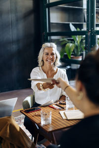 Smiling businesswoman handing over papers to colleague in loft office