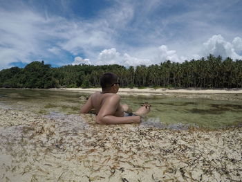 Boy sitting on lake against sky