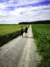 Rear view of women jogging on road amidst field against sky