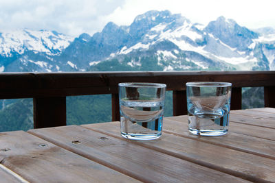 Glasses on table against snowcapped mountains