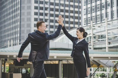 Happy business people giving high-five while standing against building