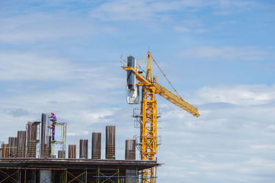 Low angle view of crane by building against sky