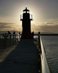 Lighthouse by sea against sky during sunset