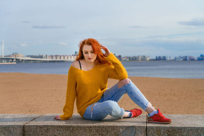 Young red-haired girl in yellow sweater and jeans. pretty woman sits