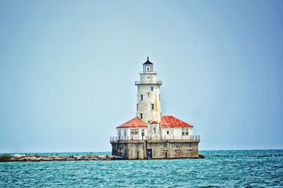 Lighthouse by sea against clear blue sky