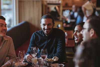 Happy multiracial male and female friends having wine in restaurant